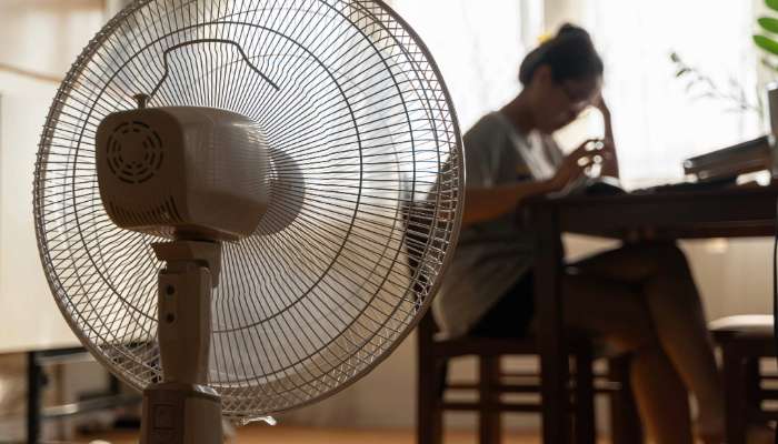 person indoors with head in hand sitting in front of a fan